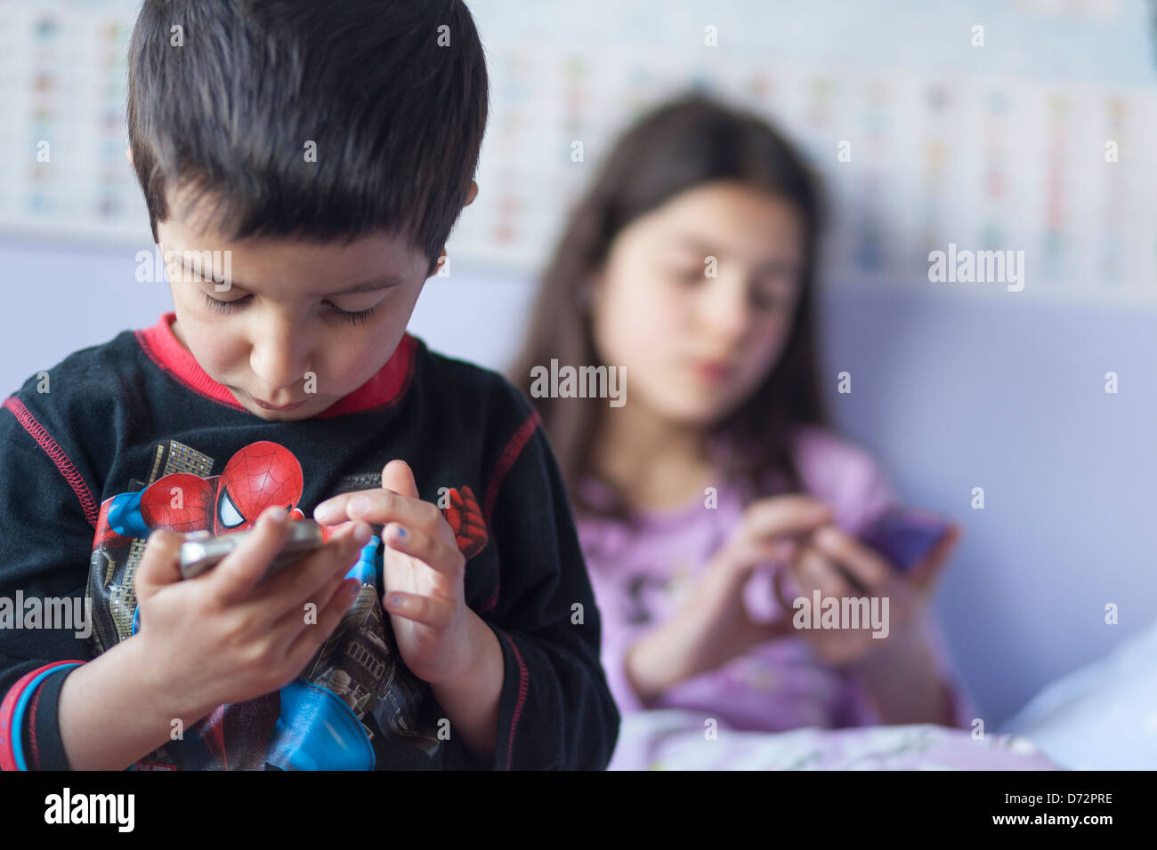 Children playing games on mobile devices in bed Stock Photo