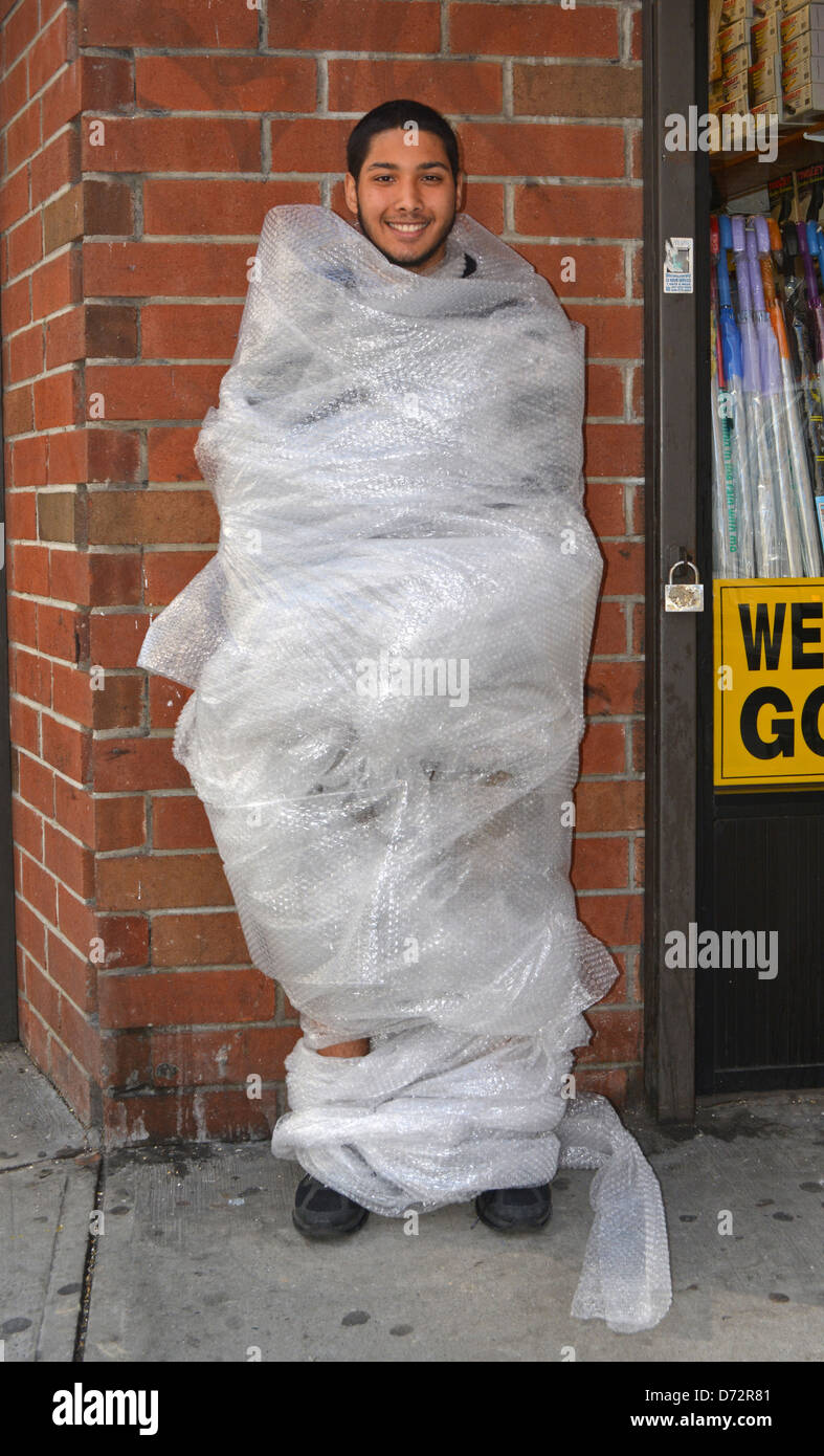 Young man wrapped in bubble wrap as part of an NYU psychology experiment which checked people's reactions.  In the East Village, New York City. Stock Photo