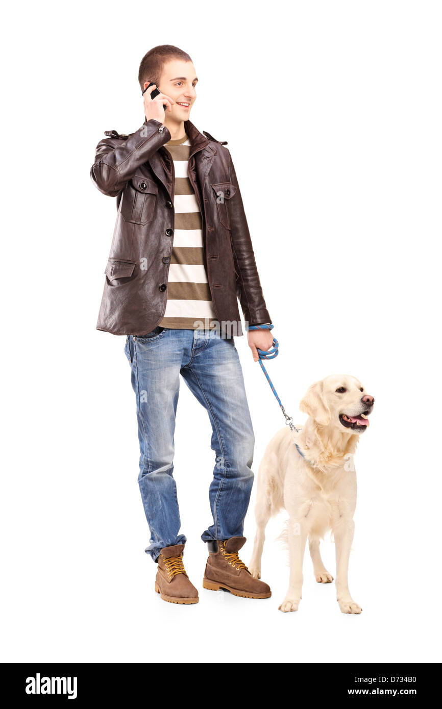 Full length portrait of a young man walking a dog and talking on a mobile phone, isolated on white background Stock Photo