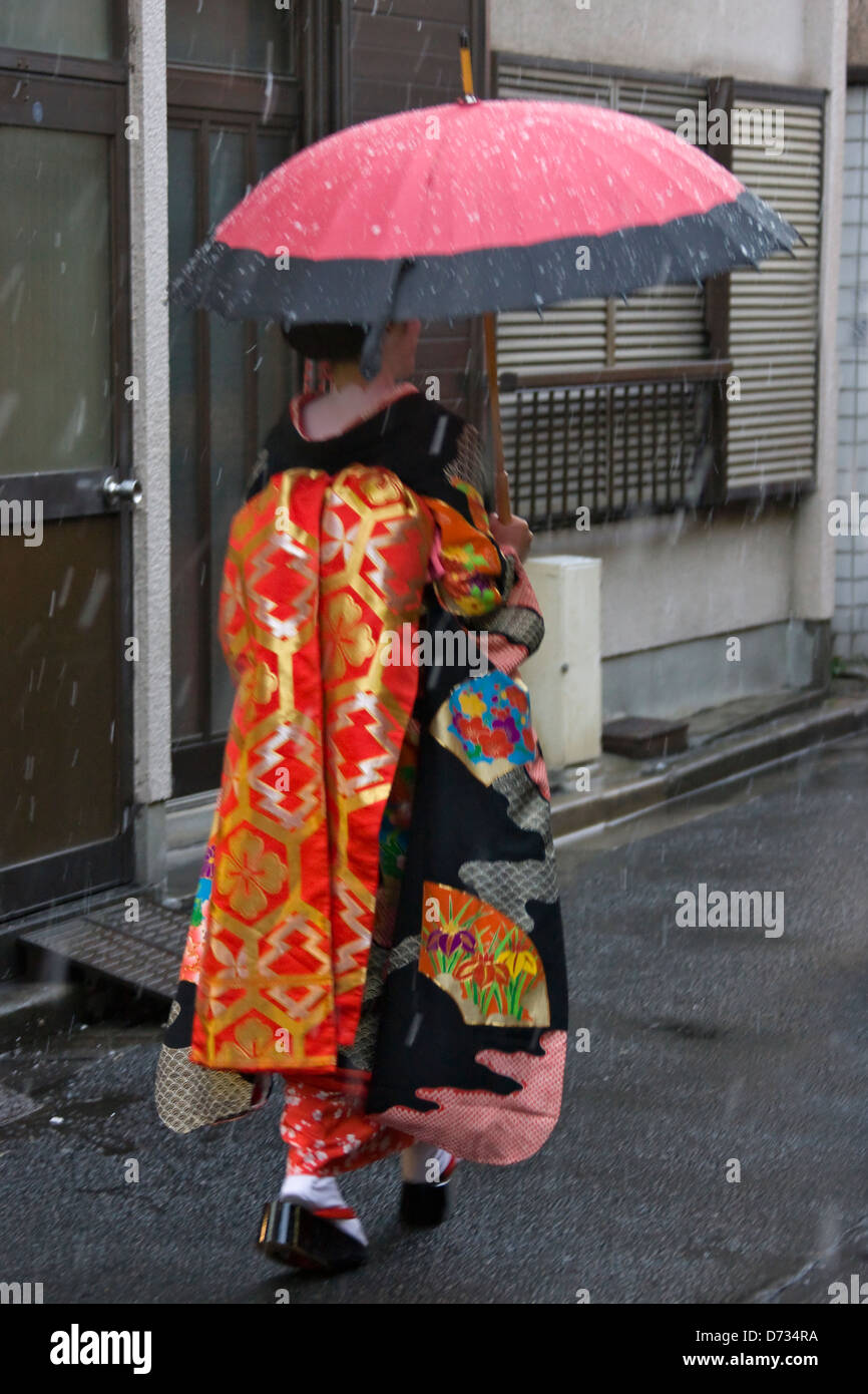 Elegant woman in traditional kimono walking with umbrella on rainy Kyoto street, showcasing the perfect blend of traditional Japanese culture and weather-ready style for kimono rental experiences
