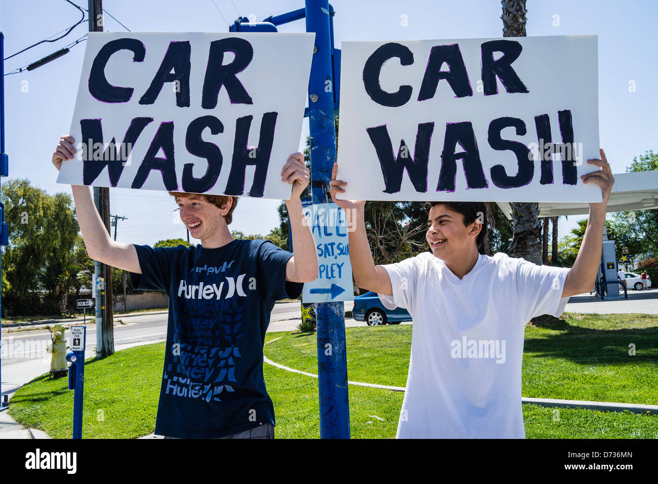 Two high school students, trying to get business, hold up signs that read 'Car Wash' at a busy intersection. Stock Photo