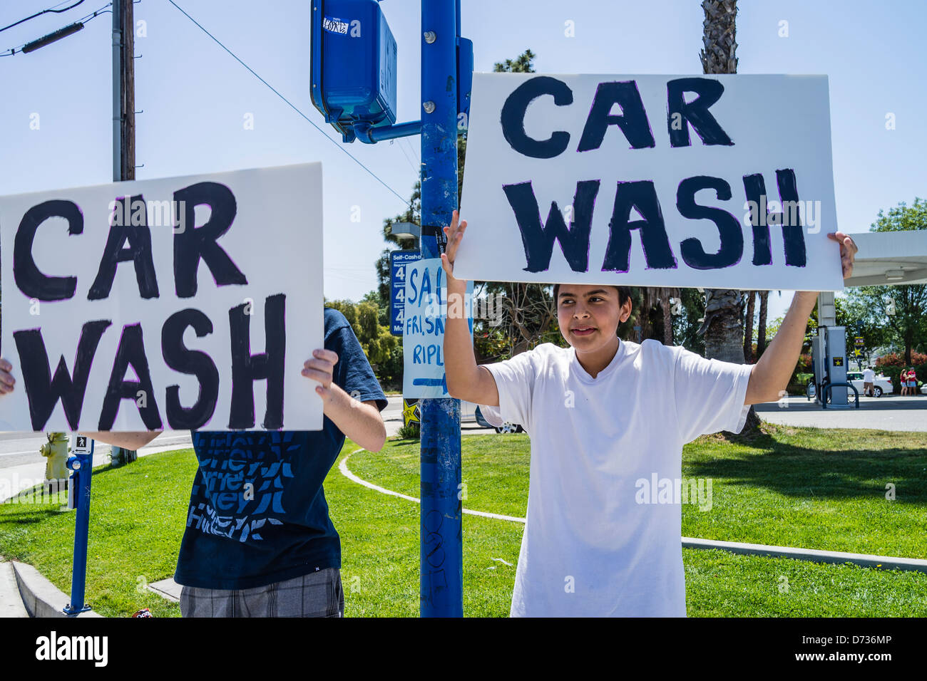 Two high school students, trying to get business, hold up signs that read 'Car Wash' at a busy intersection. Stock Photo