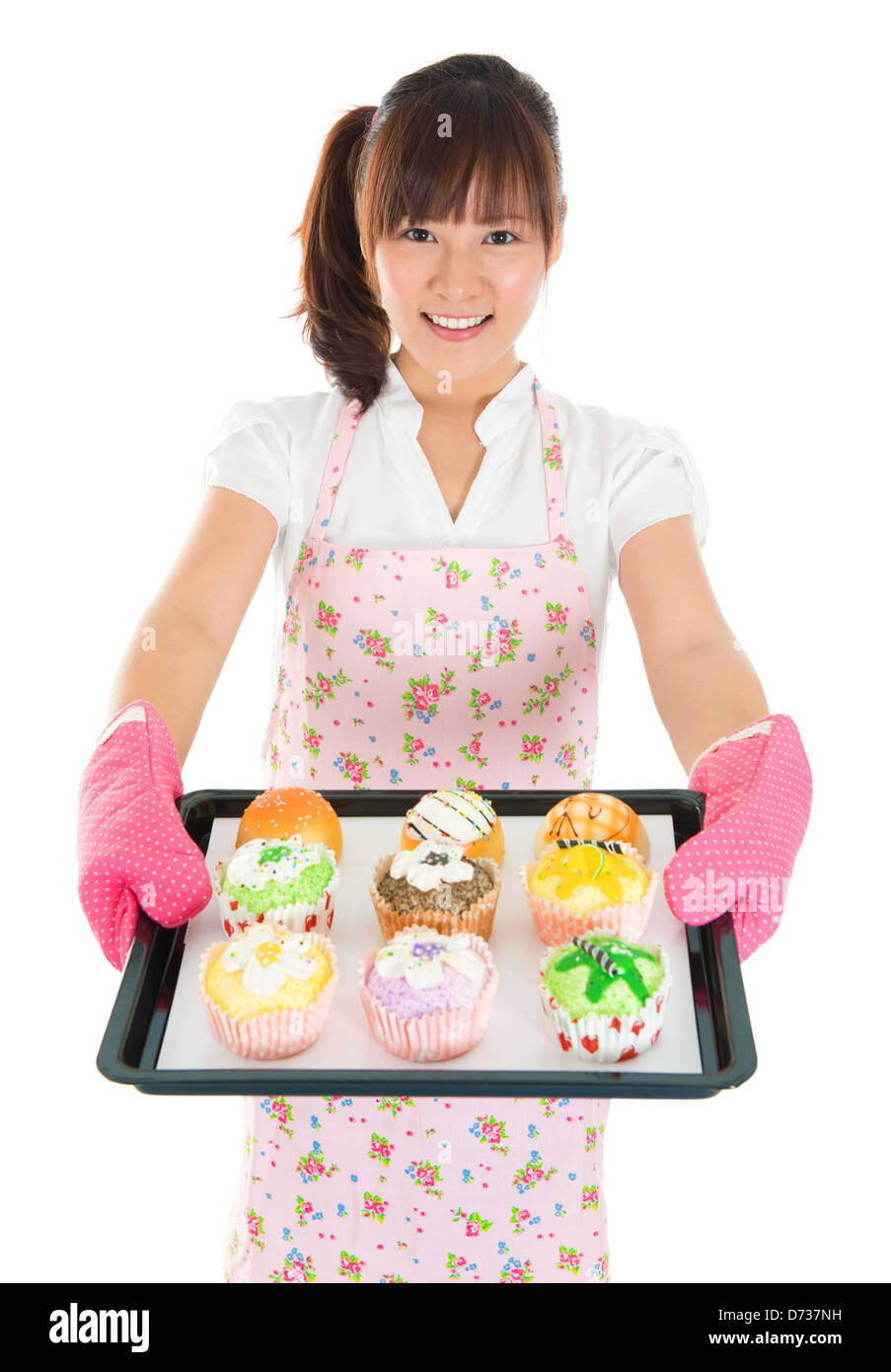 Young Asian female baking bread and cupcakes, wearing apron and gloves holding tray isolated on white. Stock Photo