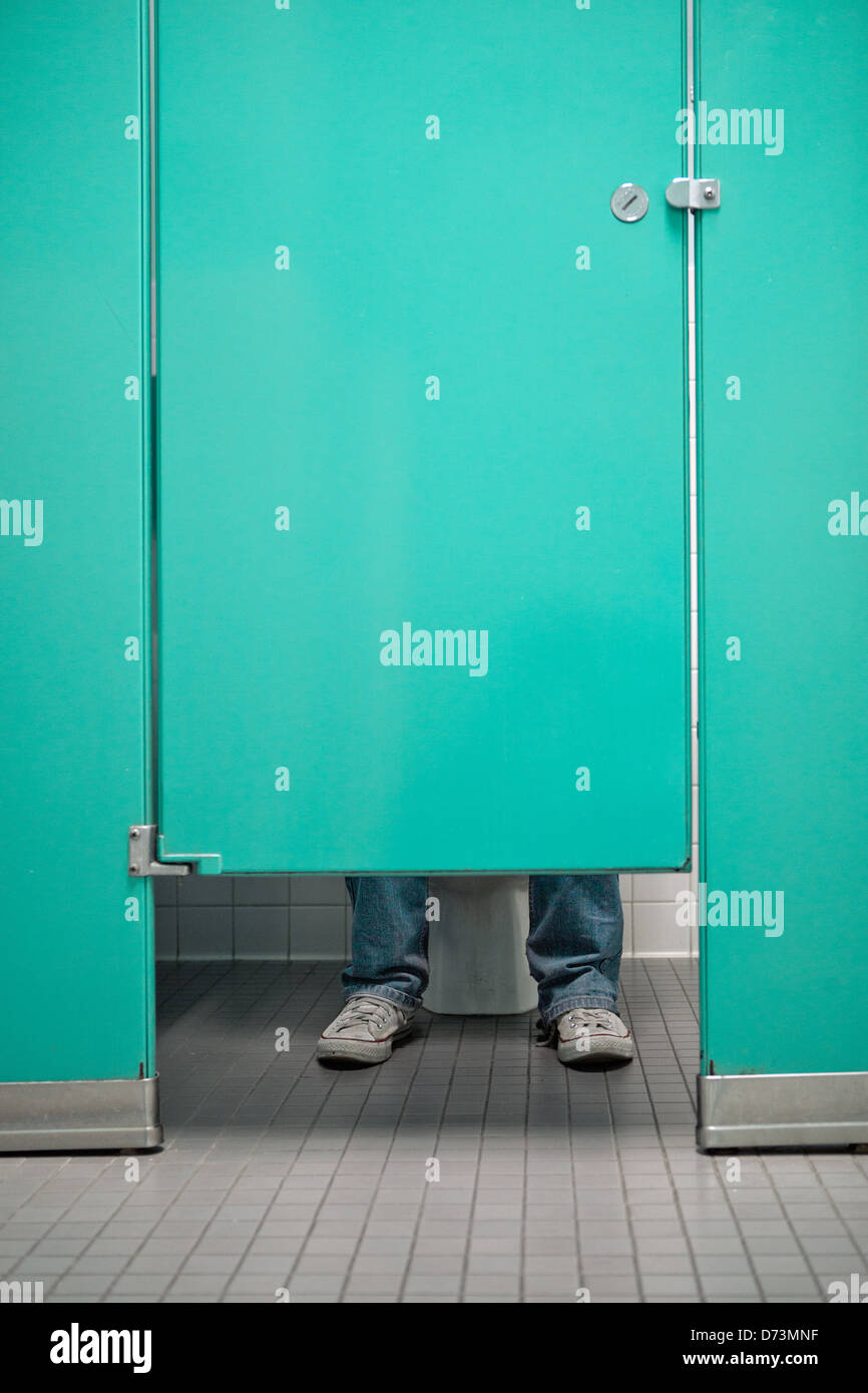 Public restroom, green door, acqua door, tennis shoes, jeans, toilet Stock Photo