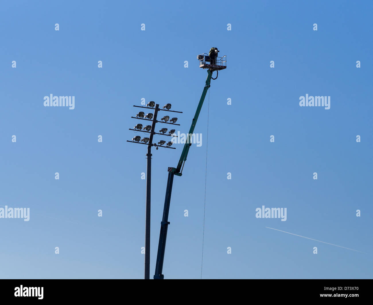 Television cameraman high in the sky on crane lift with a bank of lights nearby. Stock Photo