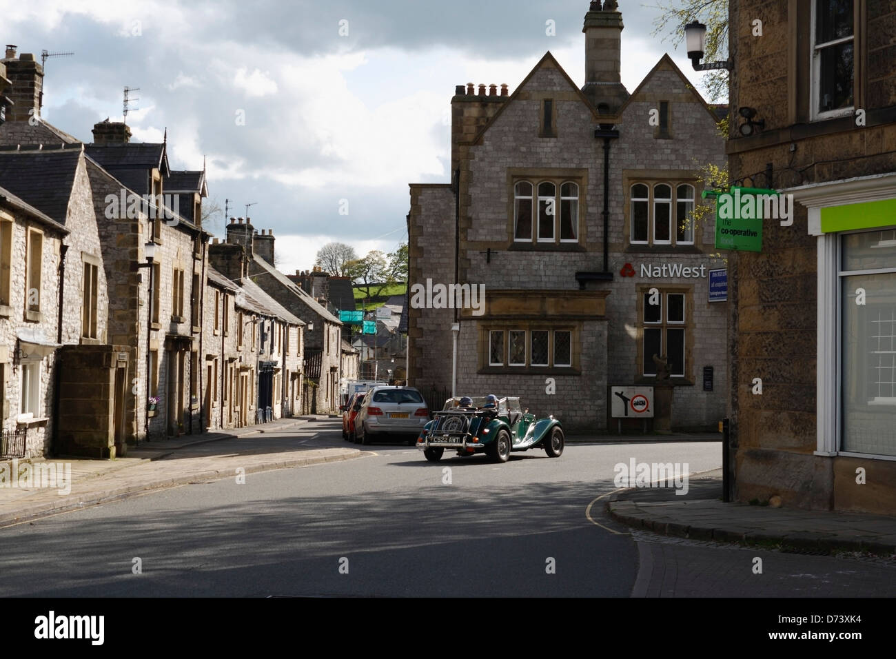 An open top car passing through Tideswell village Derbyshire England in the Peak District. Rural Britain Stock Photo