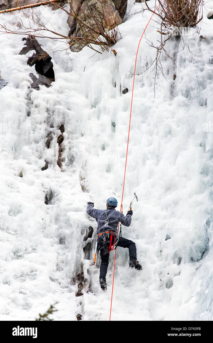 An ice climber struggles to self belay himself up a waterfall Stock