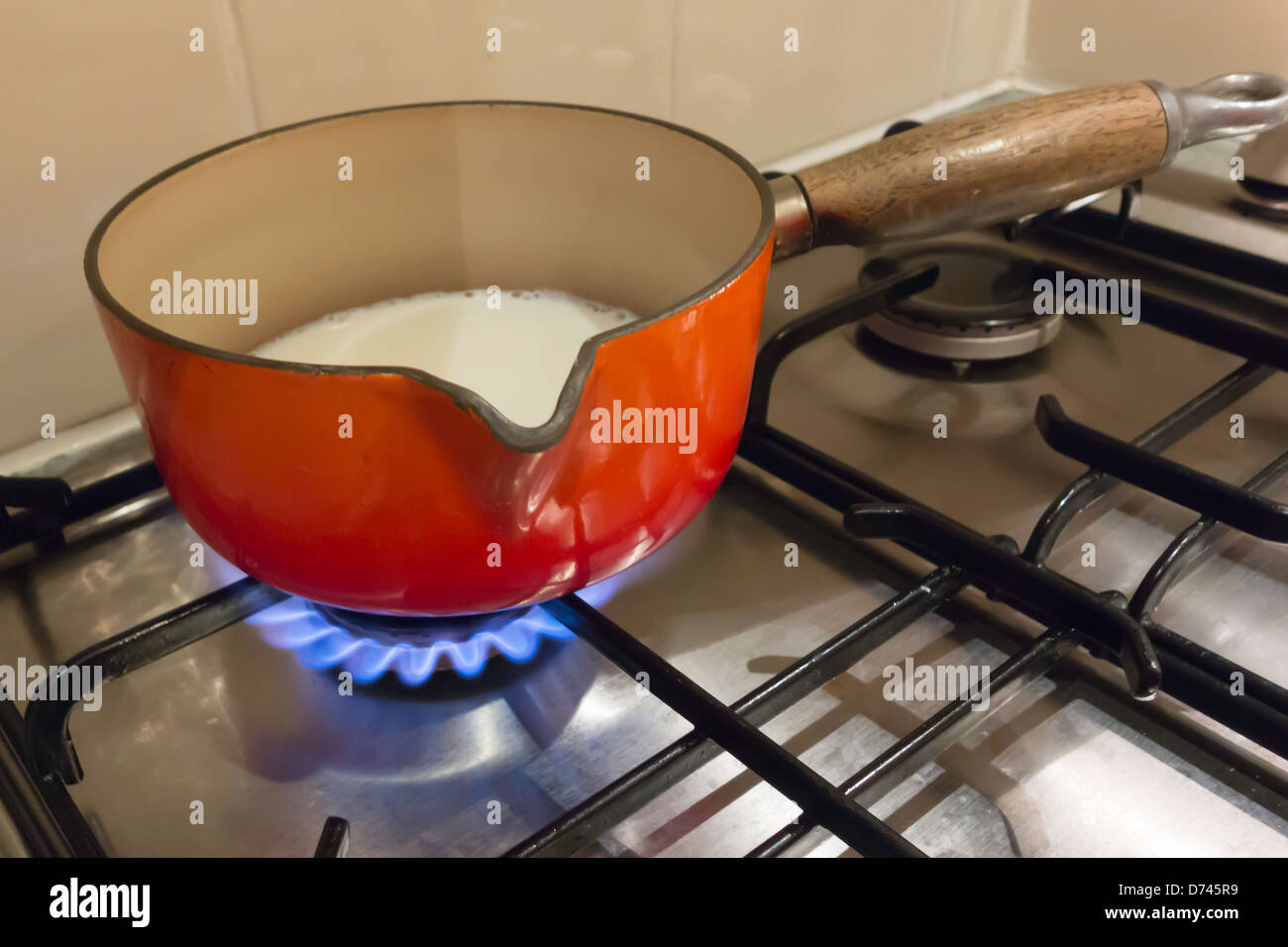 A red enameled saucepan heating milk on a gas stove Stock Photo Alamy