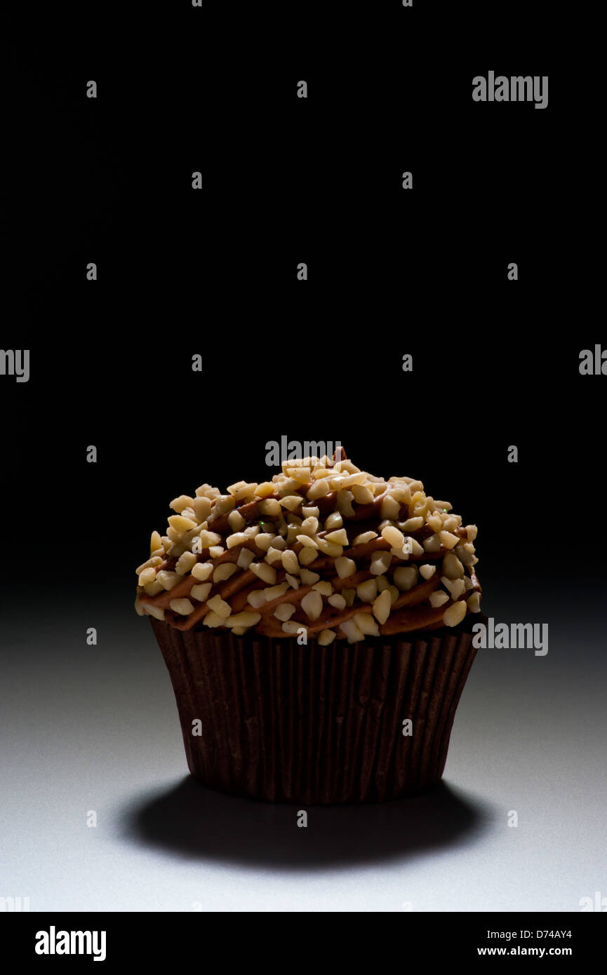 Chocolate cupcake decorated with chocolate frosting and chopped nuts on black background. Stock Photo