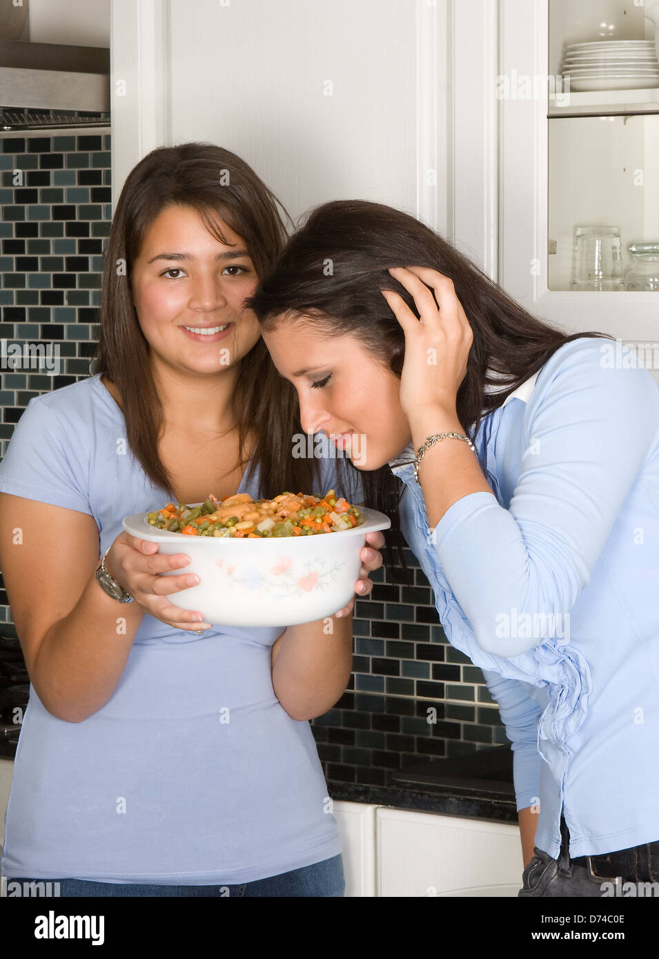 Two young women smelling food in the kitchen Stock Photo