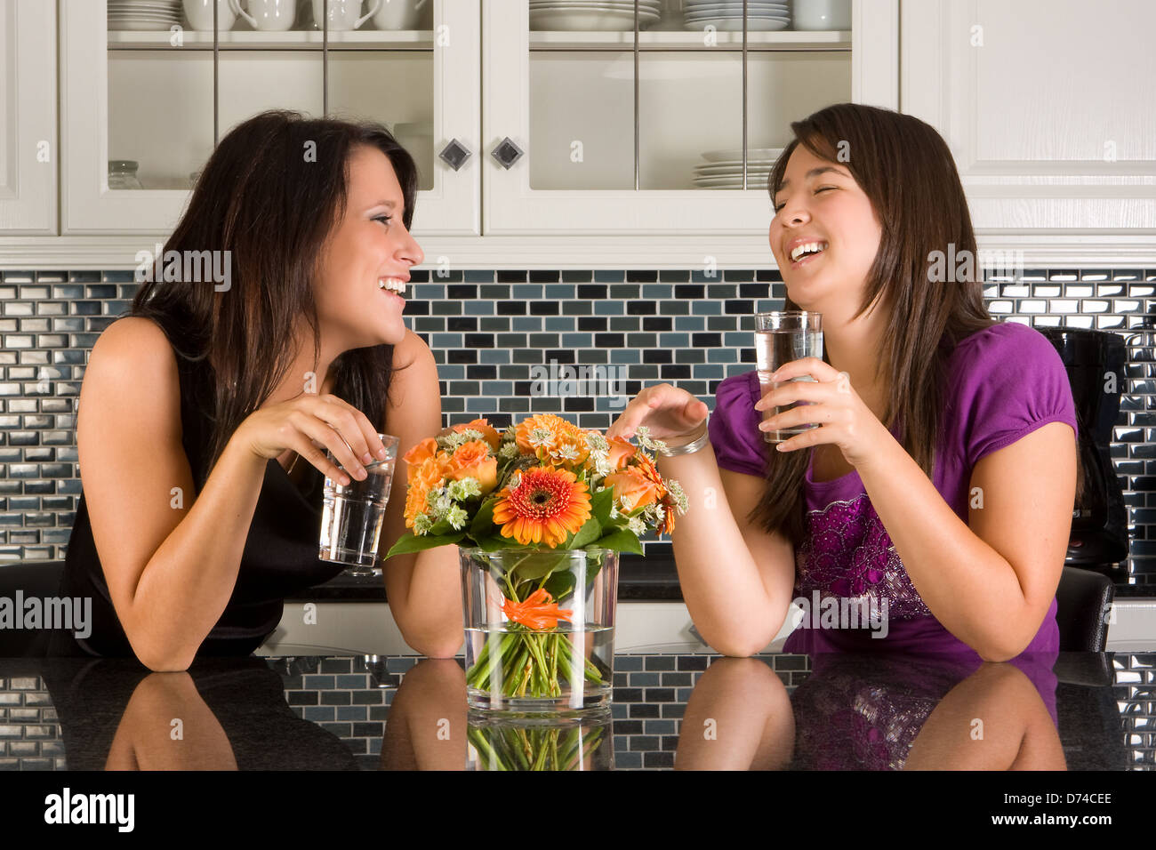 Two friends drinking water in a relaxed moment in the kitchen Stock Photo