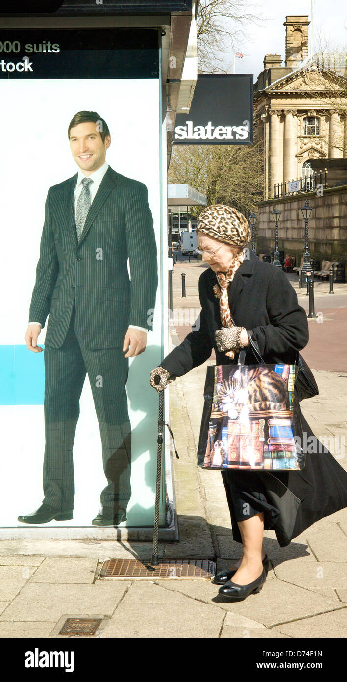 Fashionable senior women walking by clothes shop with full size picture of man in pin stripped suit  Preston city centre. Stock Photo