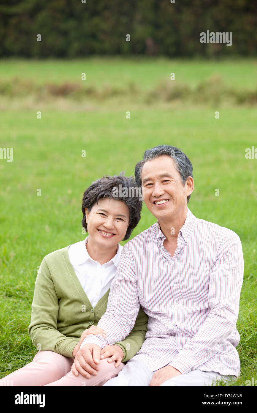 middle aged couple sitting down on empty field Stock Photo