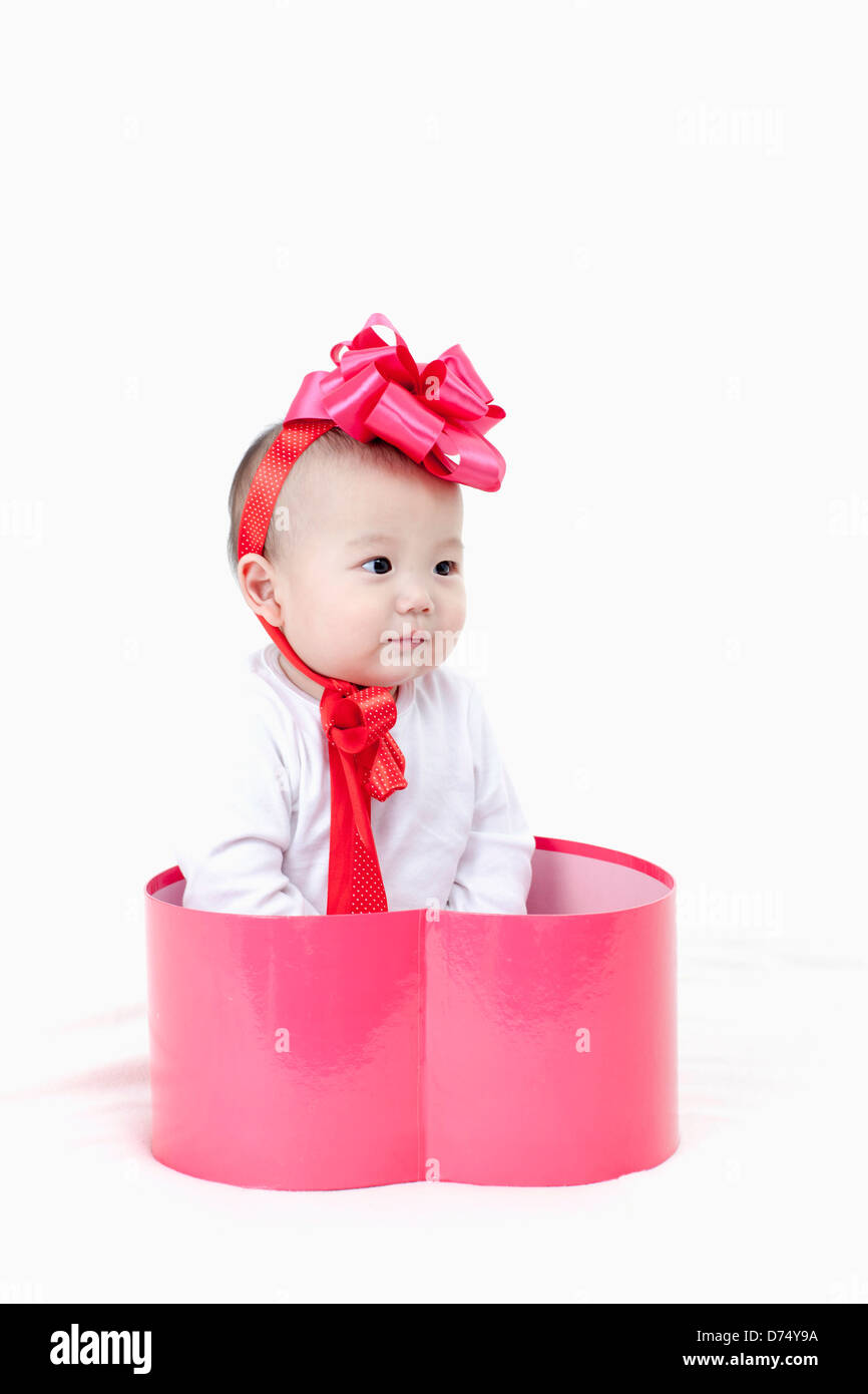 a baby inside a pink heart shaped gift box with a ribbon around head ...