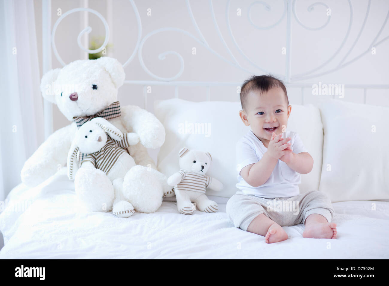 a baby sitting on a bed with teddy bear set Stock Photo - Alamy
