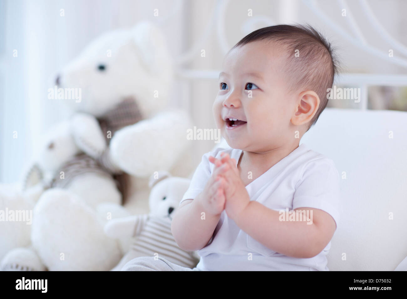 a baby sitting on a bed with teddy bear set Stock Photo - Alamy