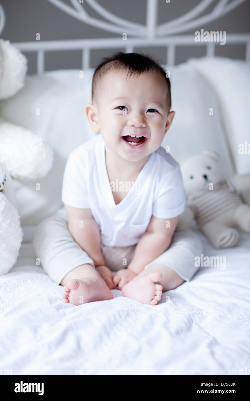 a baby sitting on a bed with teddy bears Stock Photo - Alamy