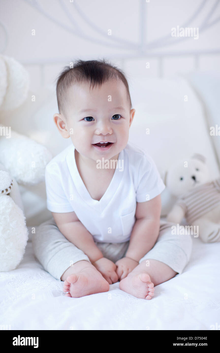a baby sitting on a bed with teddy bears Stock Photo - Alamy