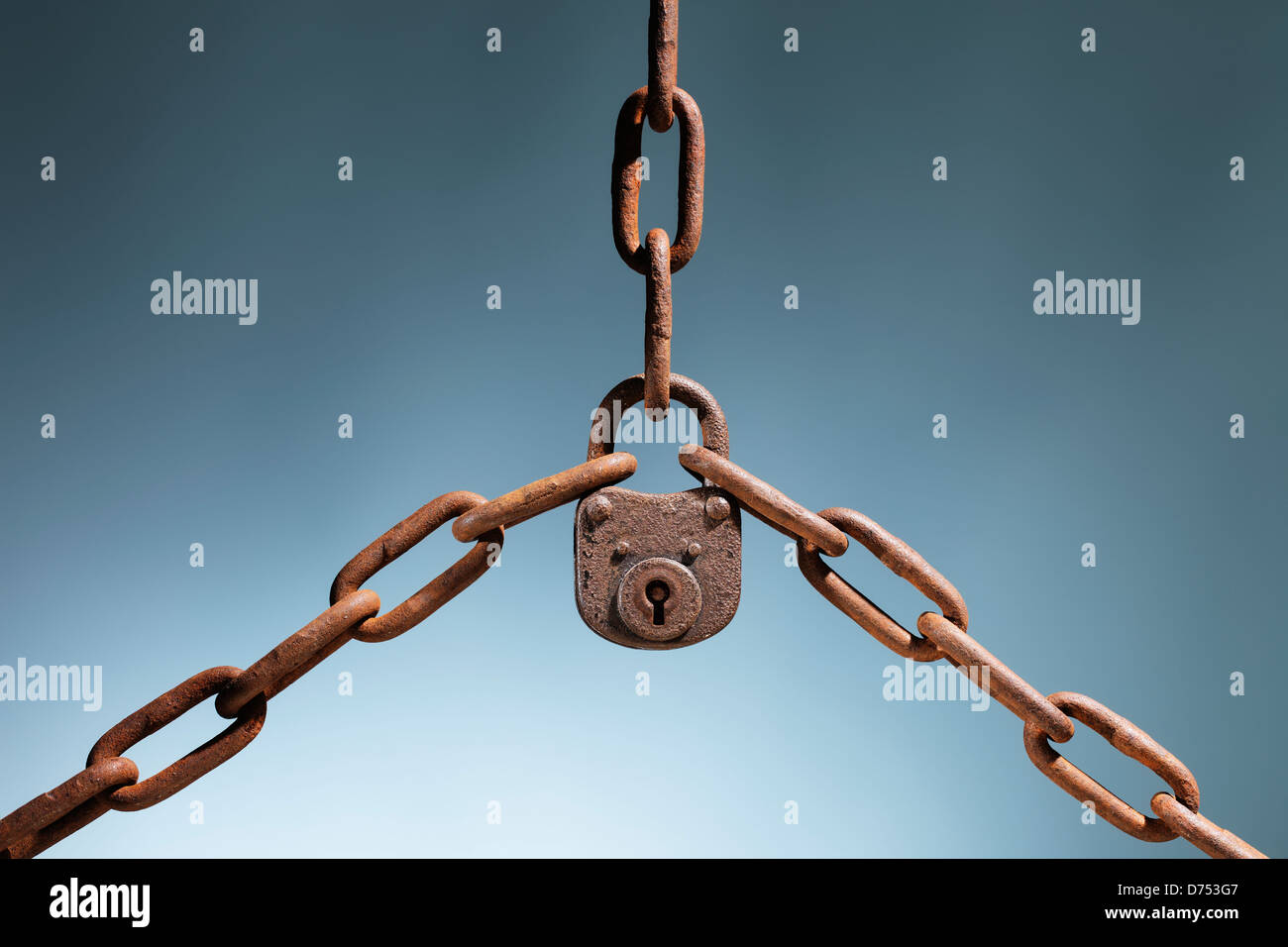 Old rusty lock holding three rusty chains together. Stock Photo