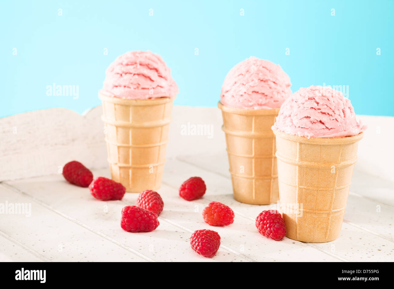 three raspberry ice cream waffle cones with raspberries on white wood