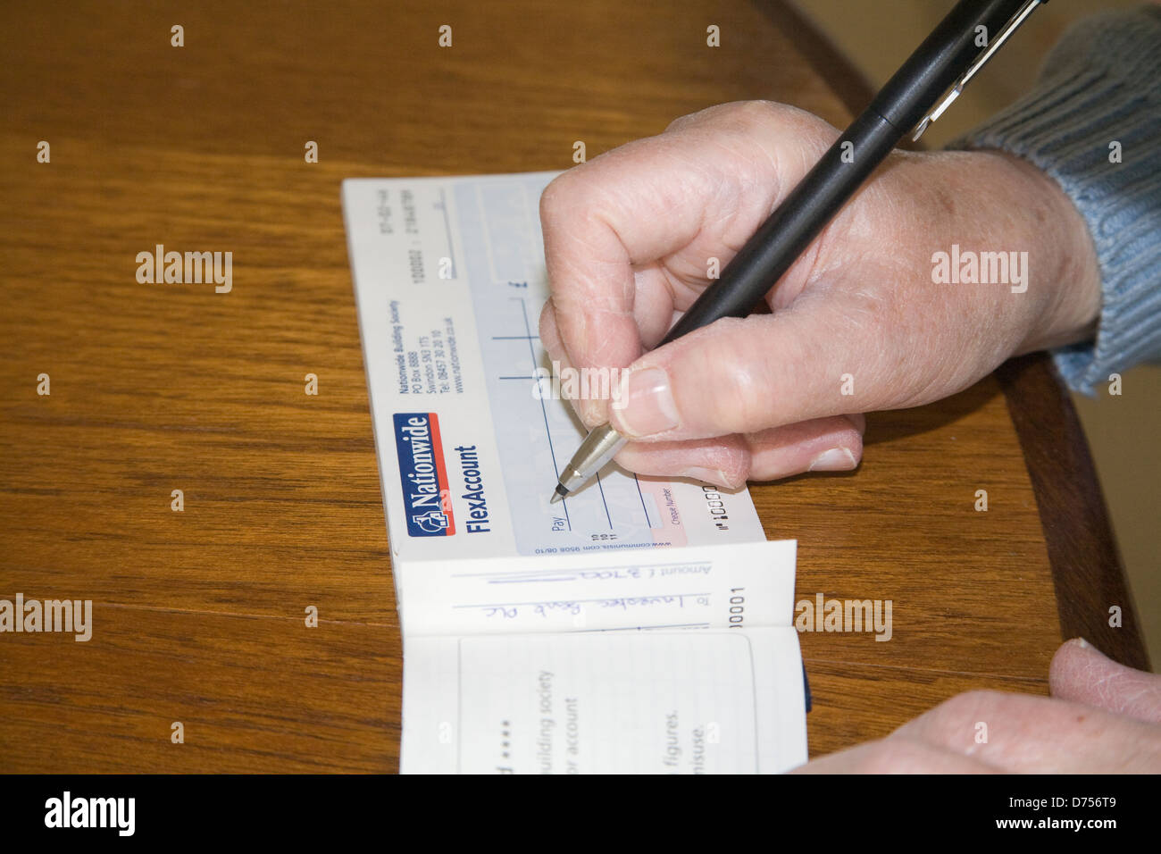 UK Elderly woman sitting at table writing a Nationwide cheque