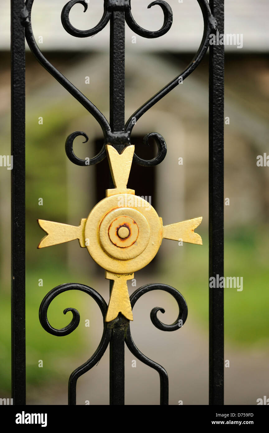 Detail of golden cross in iron gate to churchyard.  Main entrance to church in the background Stock Photo