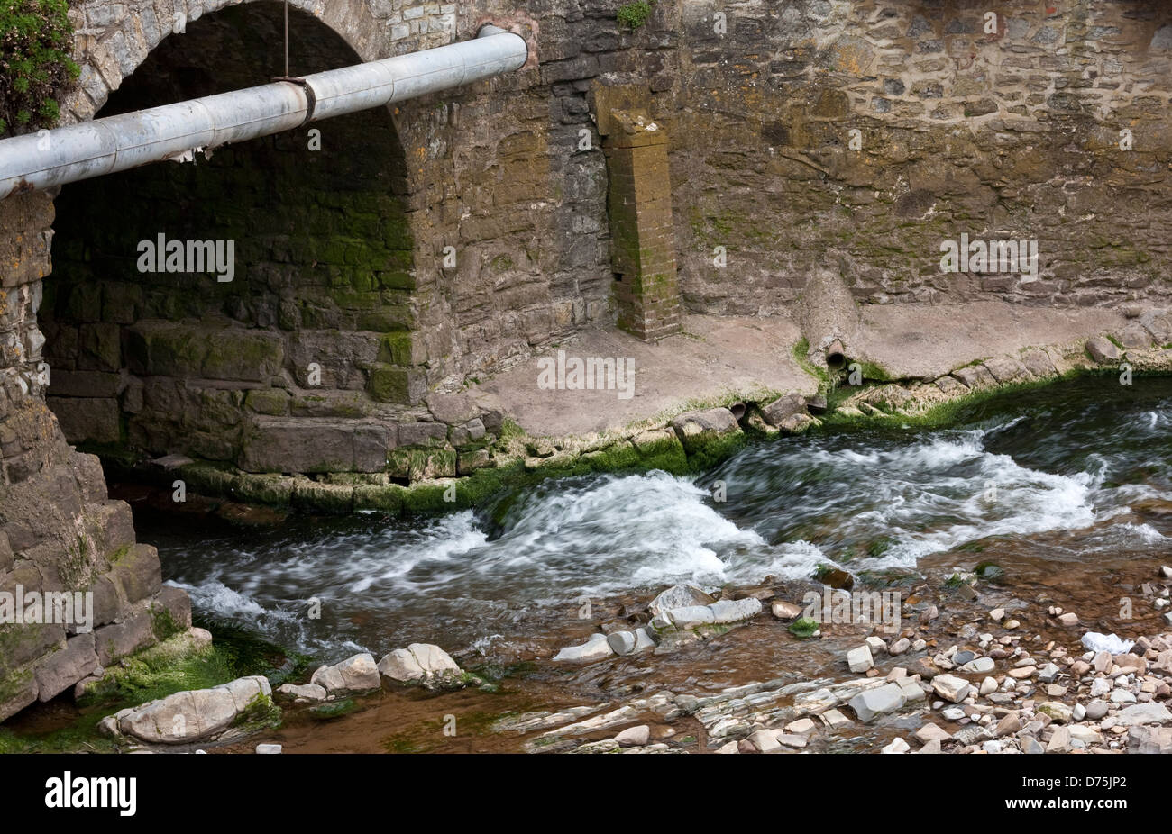 water running into a culvert with a storm drain running from the road Stock Photo