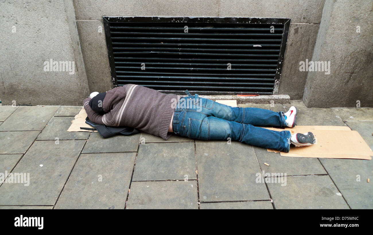 Man prostrate asleep (maybe drunk or hungover) passed out on pavement by heating vent to keep warm Swansea Wales UK KATHY DEWITT Stock Photo