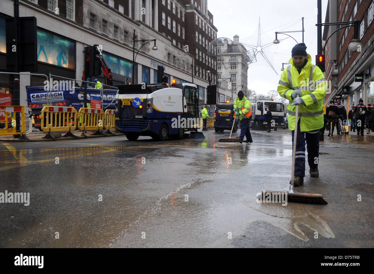 Workers clean up the street after a water main burst outside the ...