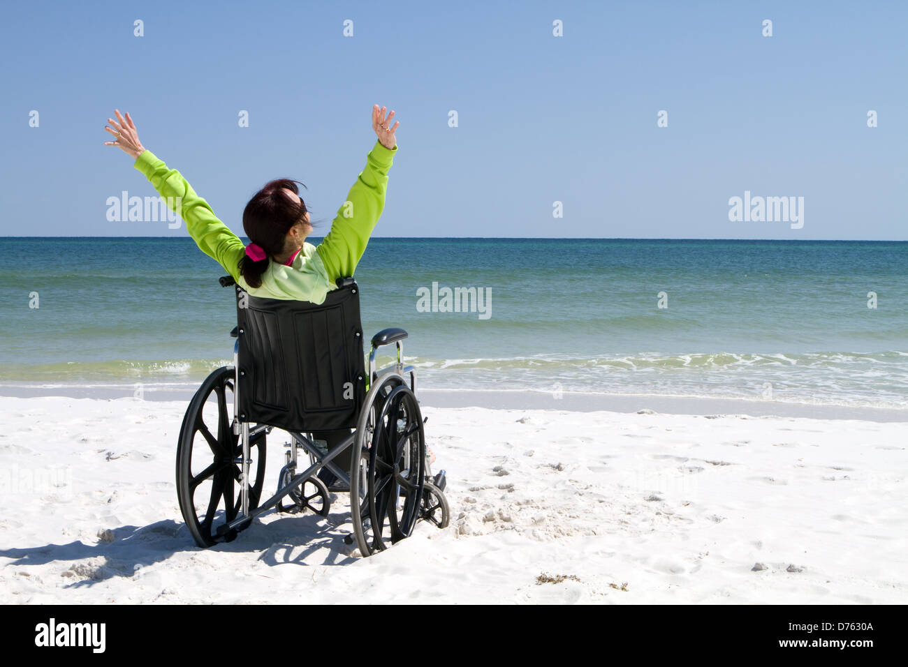 Woman with arms raised celebrates her achievement and success in the sunshine even with her disabilities in a wheelchair. Stock Photo