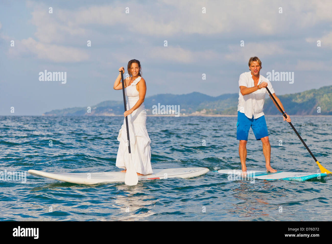 Dressed up man and woman riding paddle boards Stock Photo