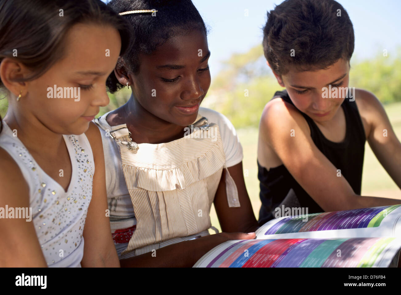 Young people and education, two little girls and one boy reading book in city park Stock Photo