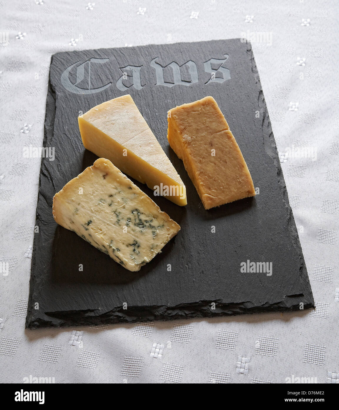 Welsh slate cheese board with 'Caws' ( Welsh for cheese ) inscribed on it with a selection of hard cheeses. Stock Photo