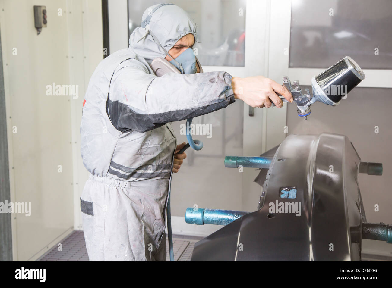 Car body painter spraying paint or color on bodywork in a garage or