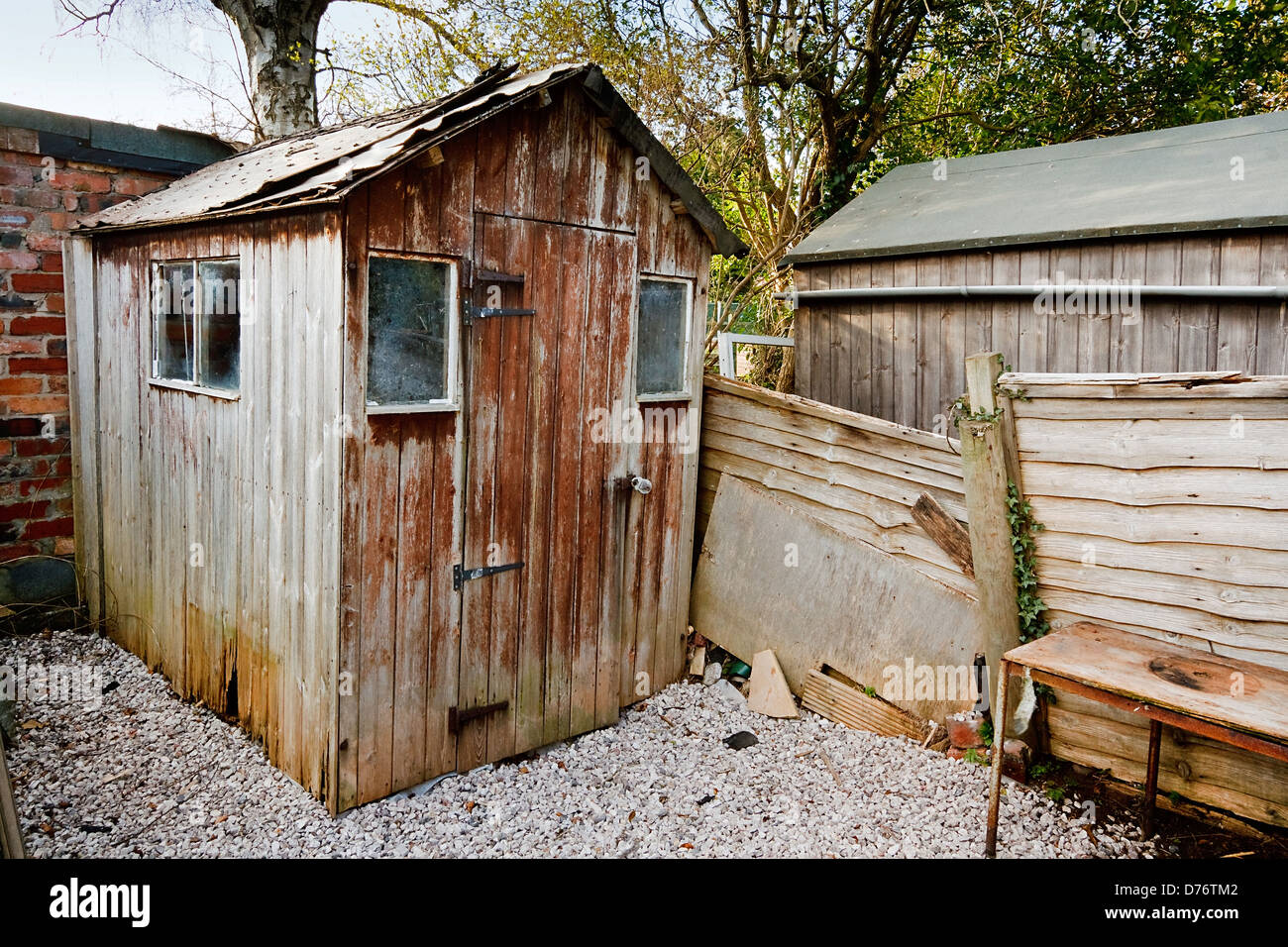 badly maintained old aged run down burlap panel wooden garden shed with damaged roof and hole from wood rot Stock Photo