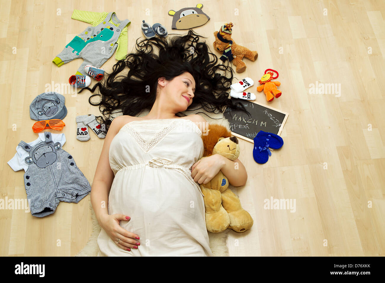 Pregnant woman surrounded with the toys and cloth for the to be born baby Stock Photo