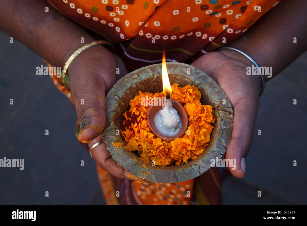 A woman holds puja pooja offerings with flowers an candle at Ganges river in Varanasi, India. Stock Photo