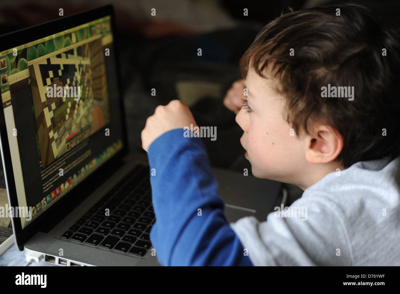 8 year old boy playing on an apple mac laptop computer in his bedroom ...