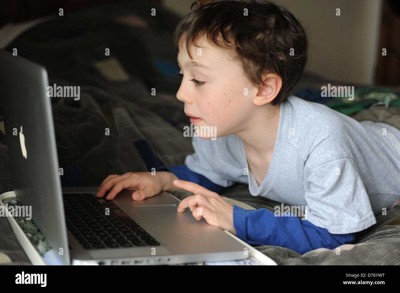 8 year old boy playing on an apple mac laptop computer in his bedroom ...