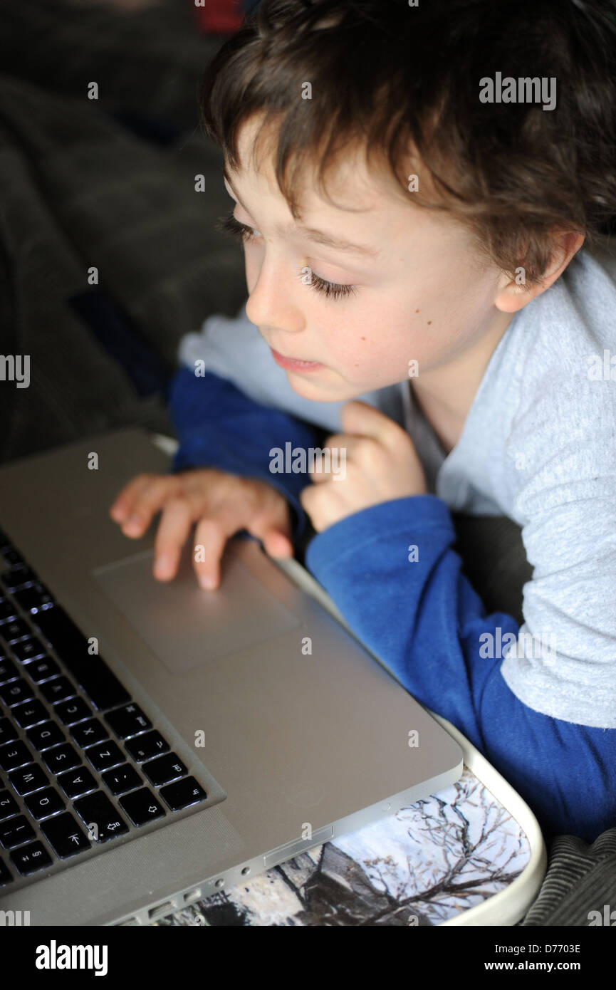 8 year old boy playing on an apple mac laptop computer in his bedroom ...