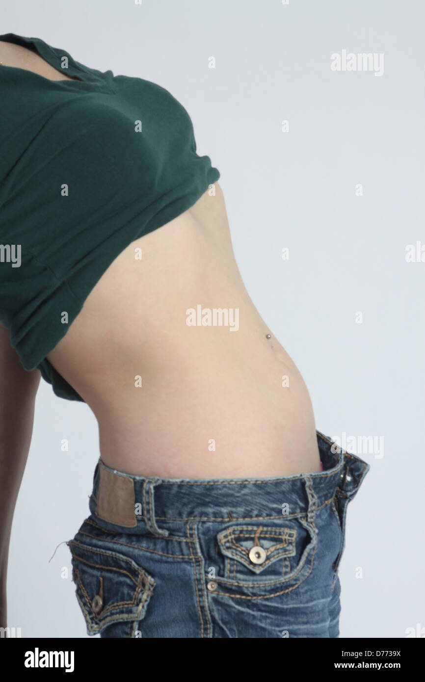 Beautiful young woman wearing a jeans  and 1/2 shirt against a light-colored  back ground, waist and midriff showing Stock Photo