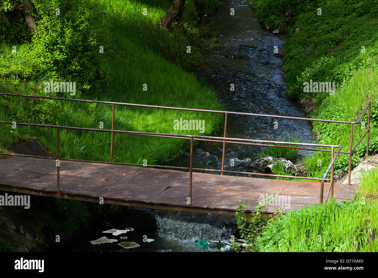 Flowing water, Spring stream bed, old rusty footbridge over the water, Outskirt Stock Photo