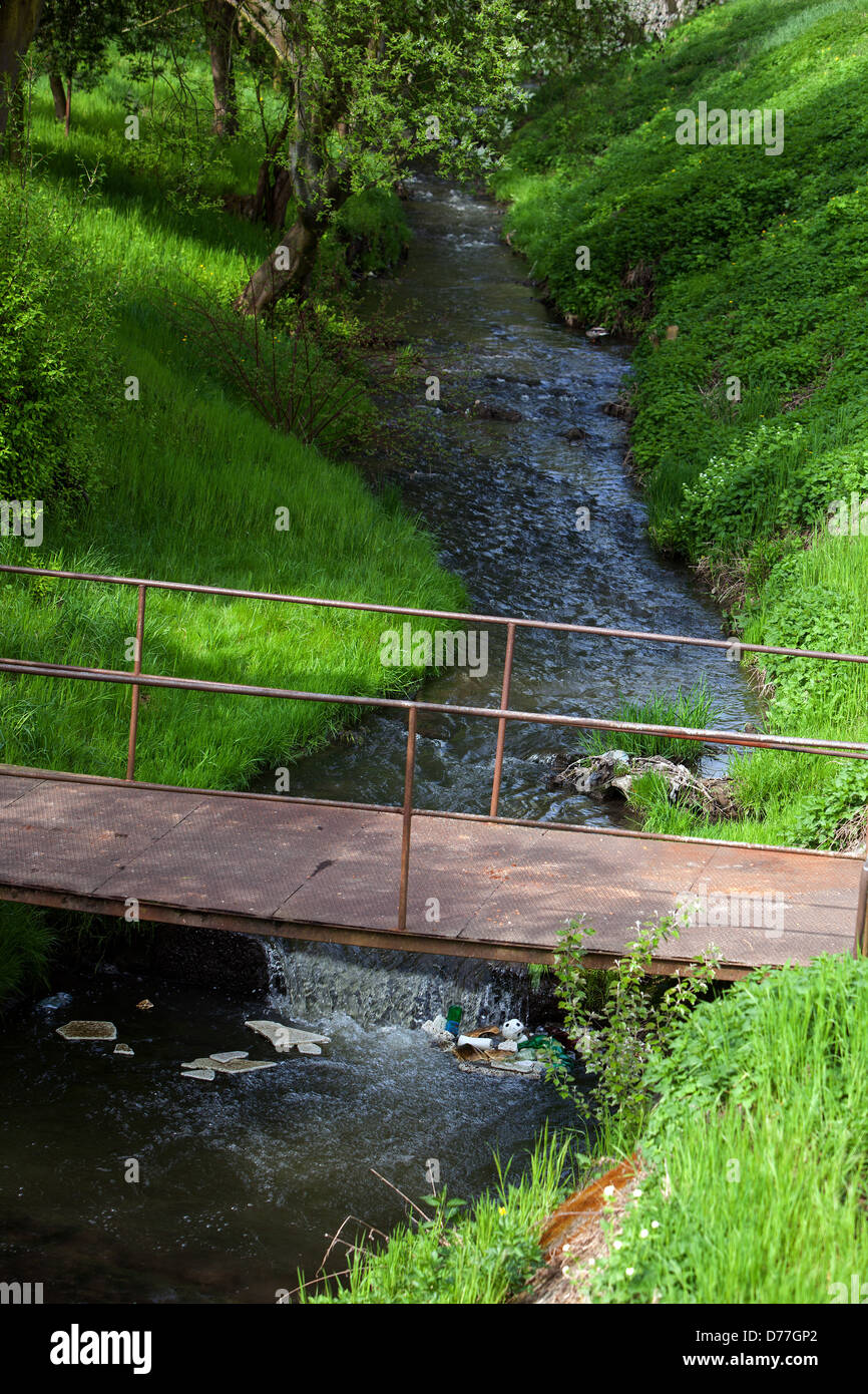 Flowing water, Spring stream bed, old rusty footbridge over the water, Suburb Stock Photo