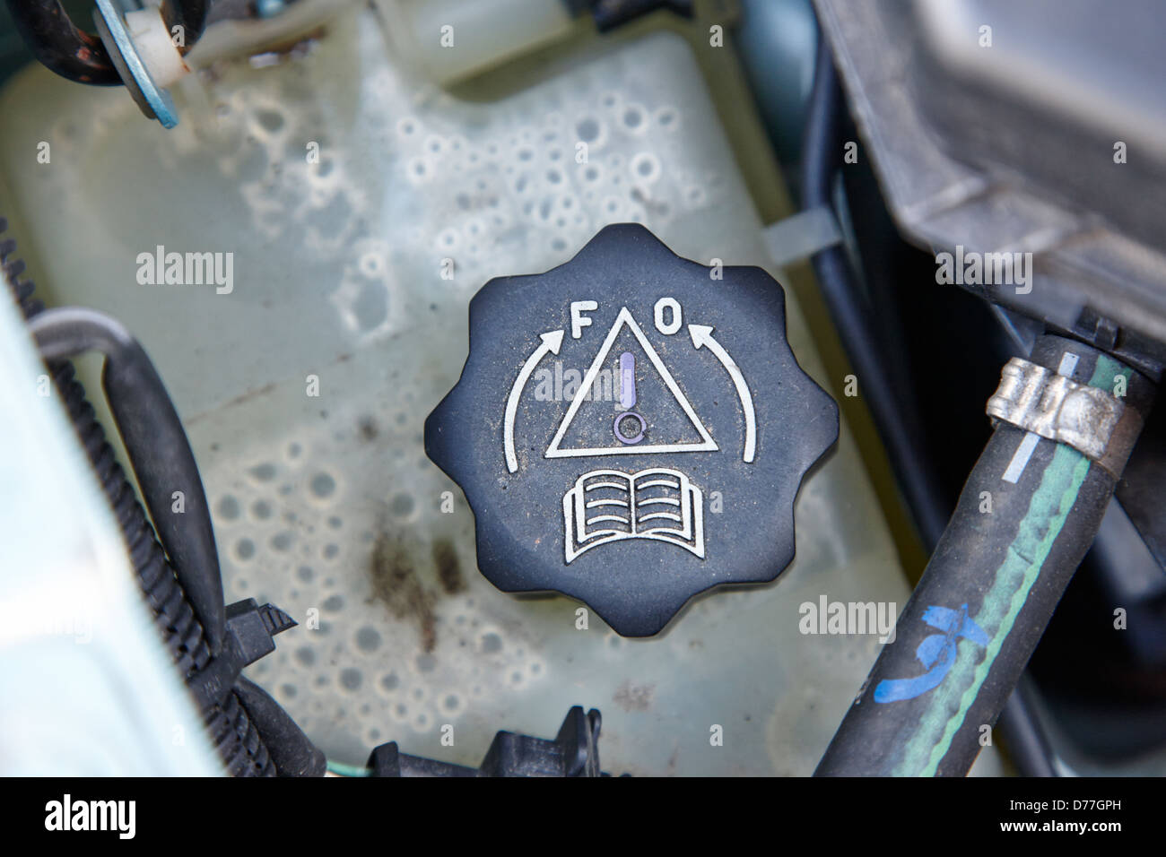 coolant system reservoir cap with warning and manual signs in a car engine compartment Stock Photo