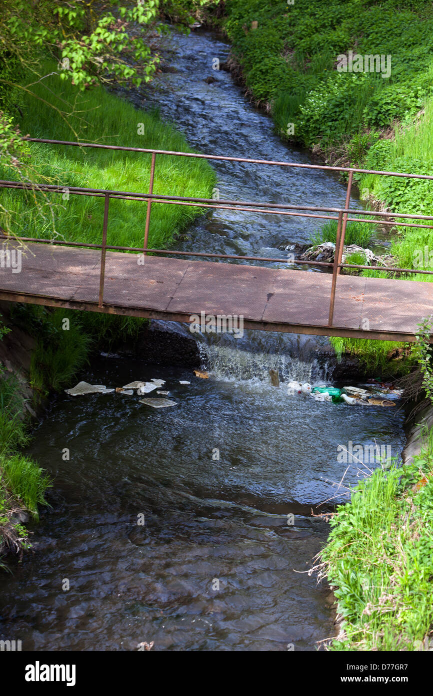 Flowing water, Spring stream bed, old rusty footbridge over the water Stock Photo
