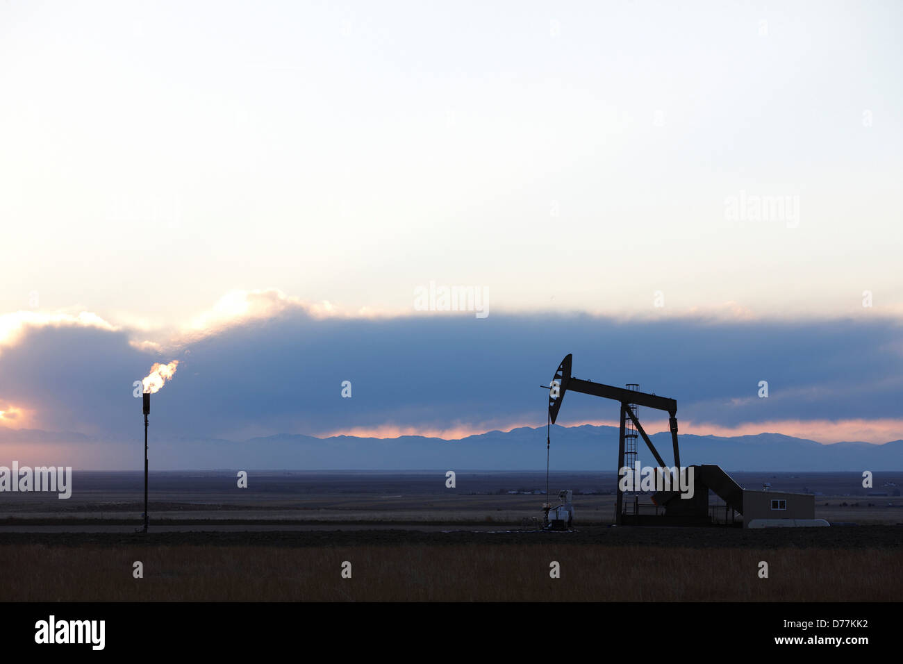 Oil well pumpjack pump jack gas flare flare stack at sunset eastern plains Colorado Rocky Mountains in distance. Stock Photo
