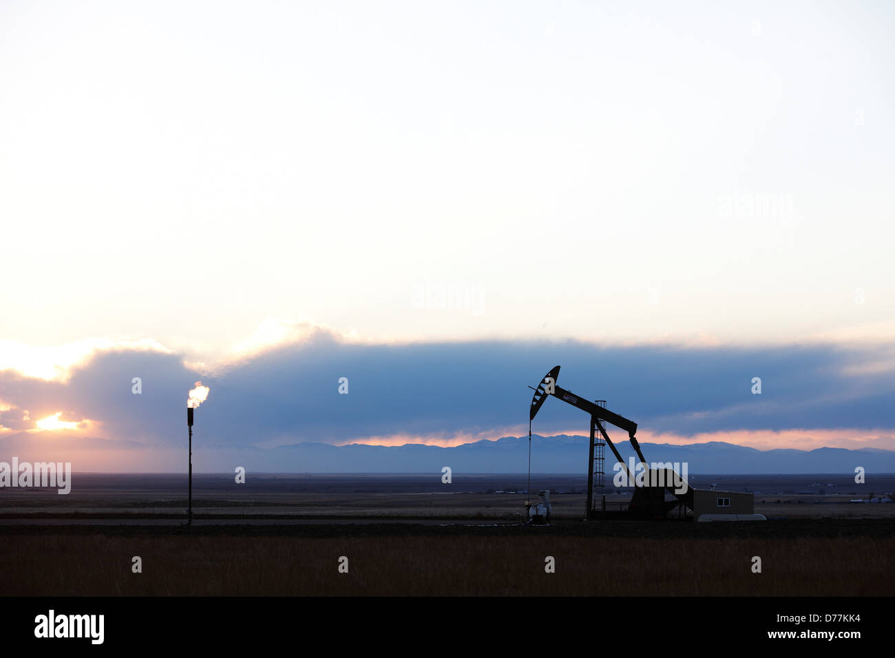 Oil well pumpjack pump jack gas flare flare stack at sunset eastern plains Colorado Rocky Mountains in distance. Stock Photo