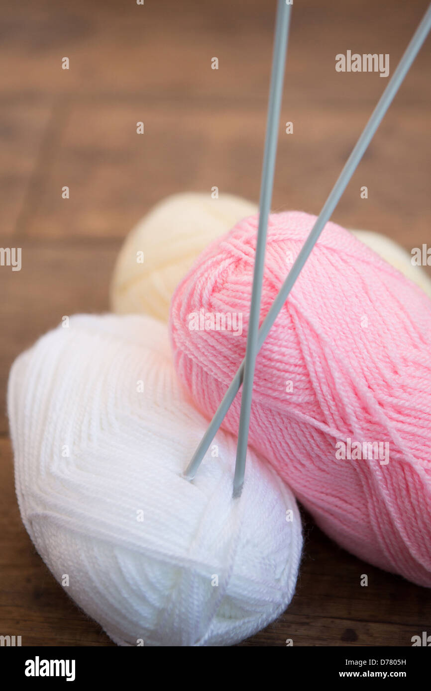 Three balls of wool with a set of knitting needles placed through one ball Stock Photo