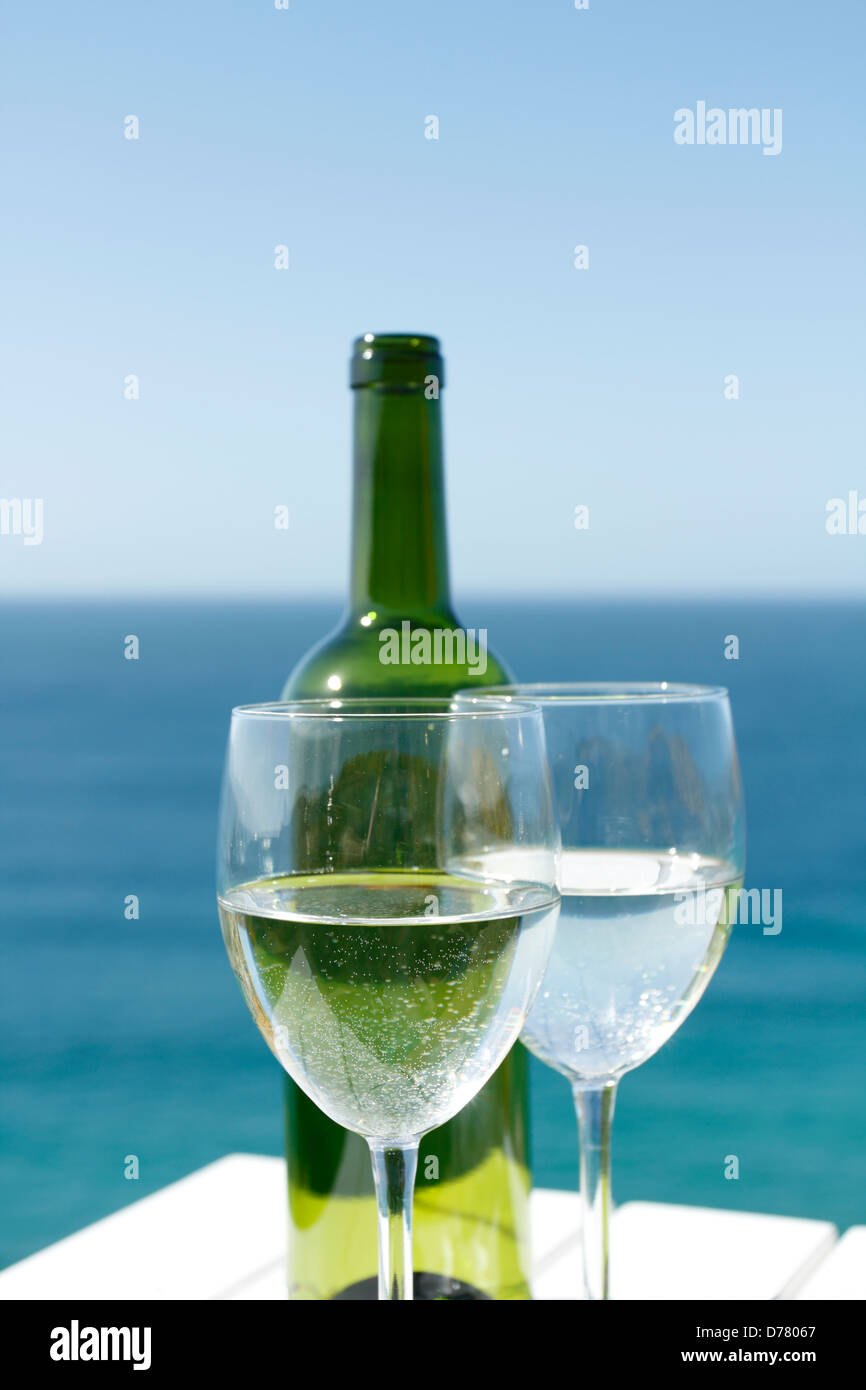 Glasses of wine on a white table by the ocean. Stock Photo