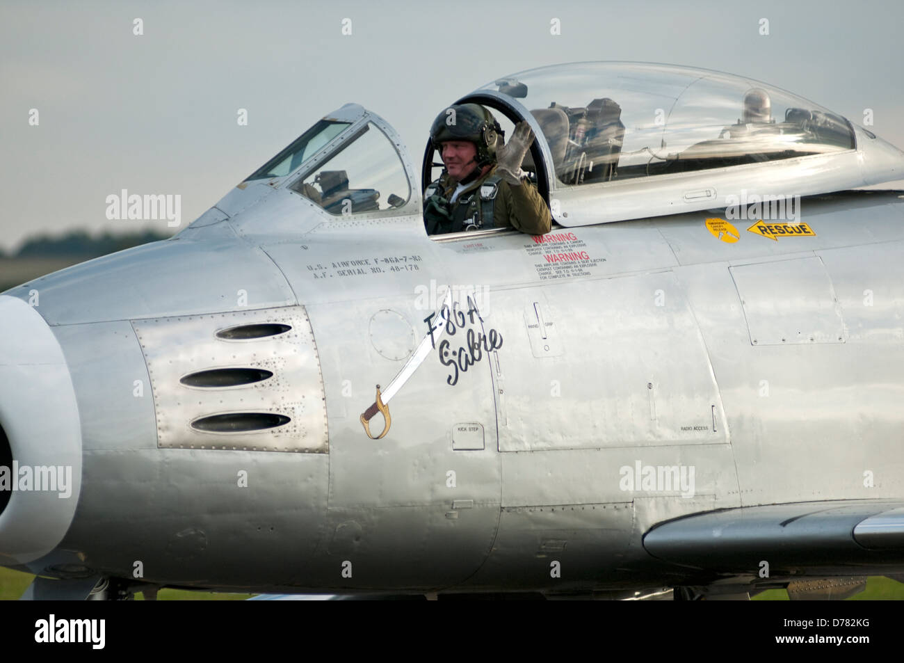 A close-up view of a 1950s USAF F86 jet fighter taxing along an airfield runway, with pilot waving. Stock Photo